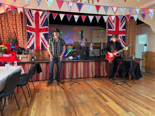 Music nights A couple of singers and musicians stand in front of the Main Hall stage singing and playing a guitar