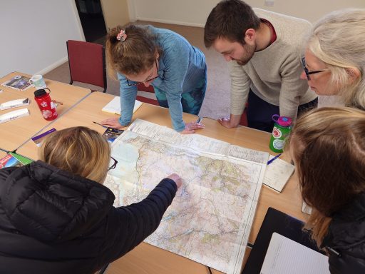 Navigation courses A group of 5 people are looking closely and pointing at a map on a table