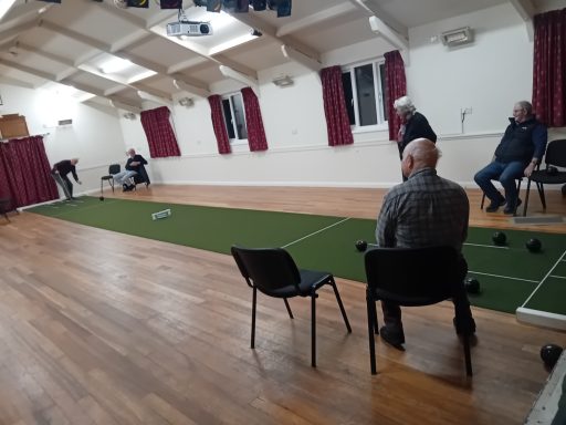 Indoor Bowls Club A group of bowls players look on as a fellow player lines up his shot on an indoor carpeted track