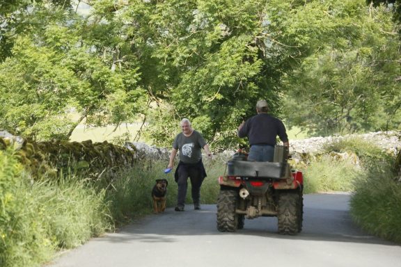 Rural community A man on a quad bike passes another man walking his dog on a country lane above Bampton, Cumbria the Lake District
