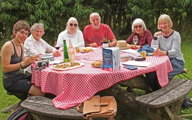 French speaking club A group of 6 people sit at a picnic table enjoying a french speaking class with a young french lady